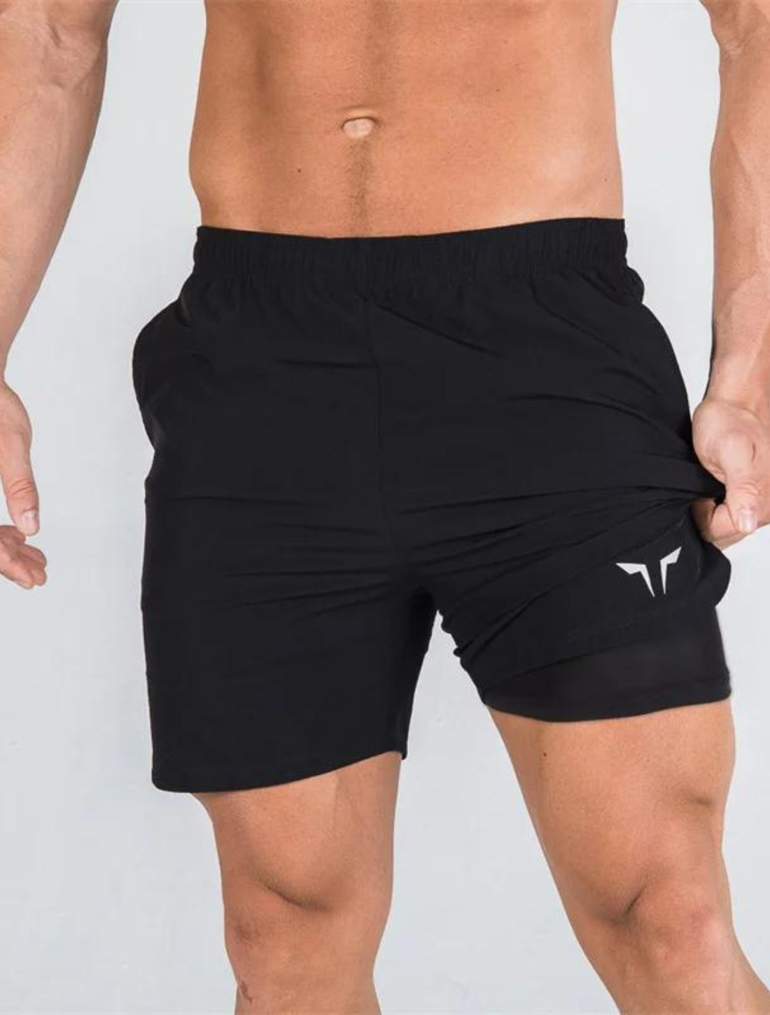 Homem vestindo o Short preto, com design 2 em 1 que combina camada externa leve e camada interna compressiva. Ideal para suporte e desempenho em treinos.