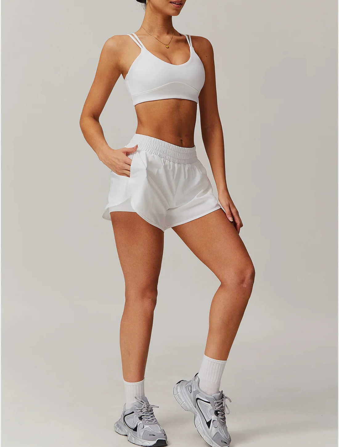 Mulher vestindo o Conjunto Maitê branco, composto por top de alças duplas e short com cintura elástica e bolsos laterais. Look moderno, ideal para treinos ou uso casual.






